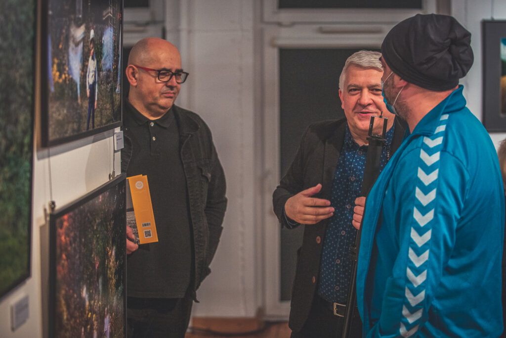 Zdjęcie. Trzech mężczyzn rozmawia na wystawie fotografii Andrzeja Borysa.