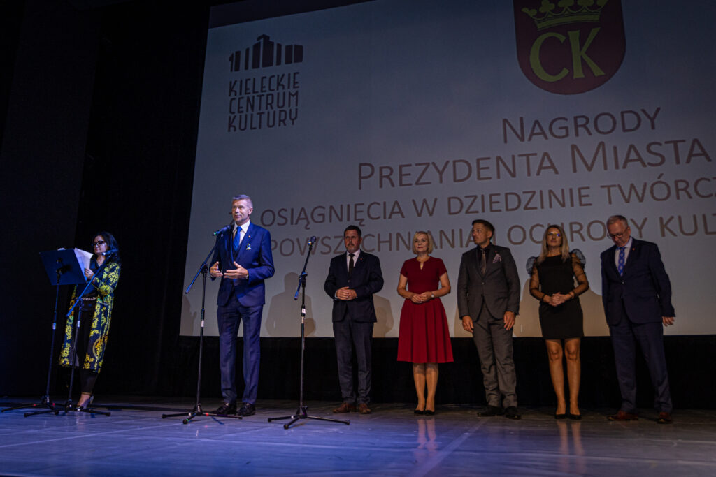 Zdjęcie. Nogdan wenta mówi do mikrofonu. W tle przedstawiciele władz miasta i olbrzymi ekran.
