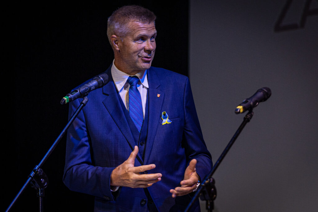 Zdjęćie. Bogdan Wenta w niebieskim garniturze mówi do mikrofonu.