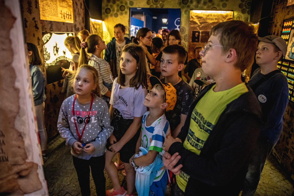 Zdjęcie. Dzieciaki z Lata w teatrze stoją w półkolu w sali Muzeum Zabawek i Zabawy.