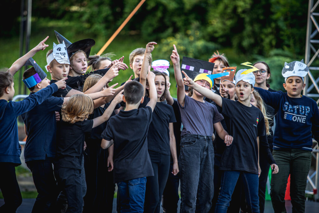 Zdjęcie. Duża grupa dzieci unosi do góry prawe dłonie z wystawionym palcem wskazującym.