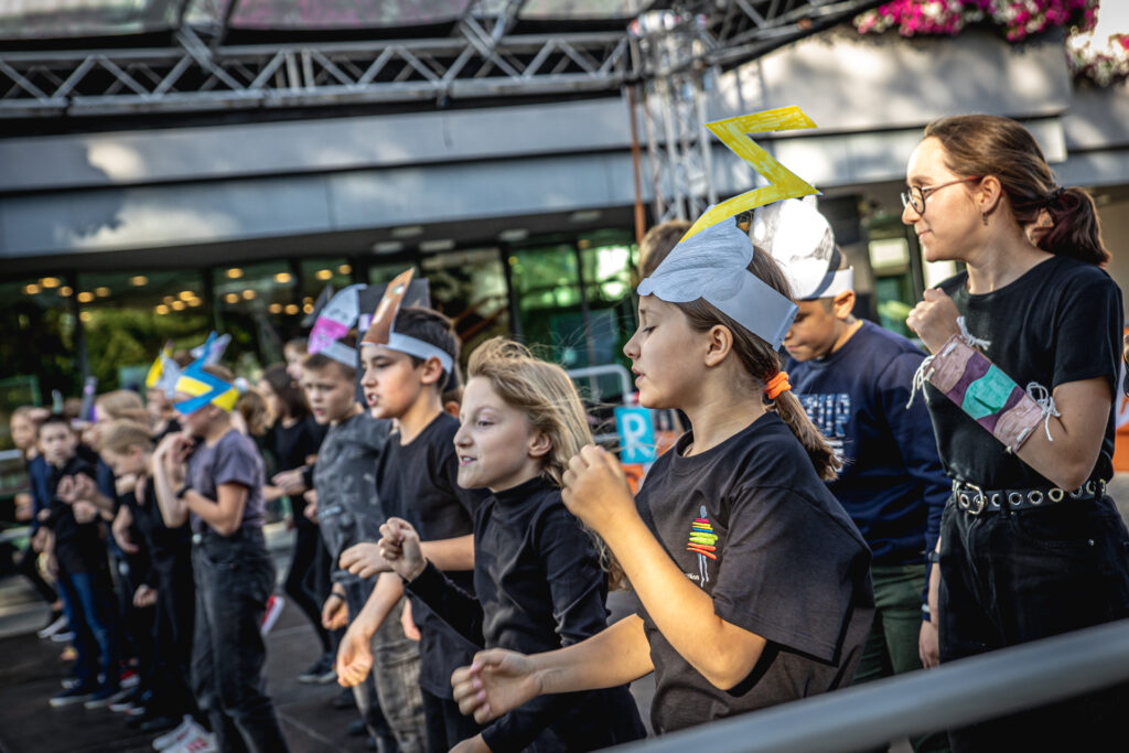 Zdjęcie. Grupa dzieci w długim rzędzie stoi na Scenie Letniej KCK.