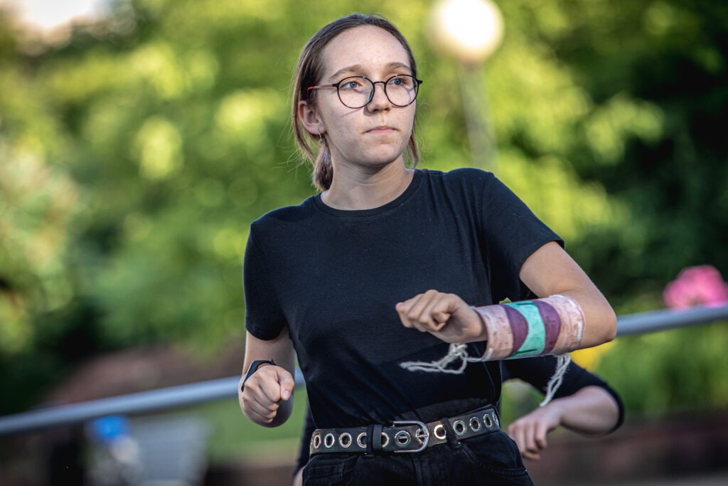 Zdjęcie. Uczestniczka lata w teatrzepatrzy w swoją lewą stronę. Ręce zgięte w łokciu, dłonie zaciśnięte w pięść.