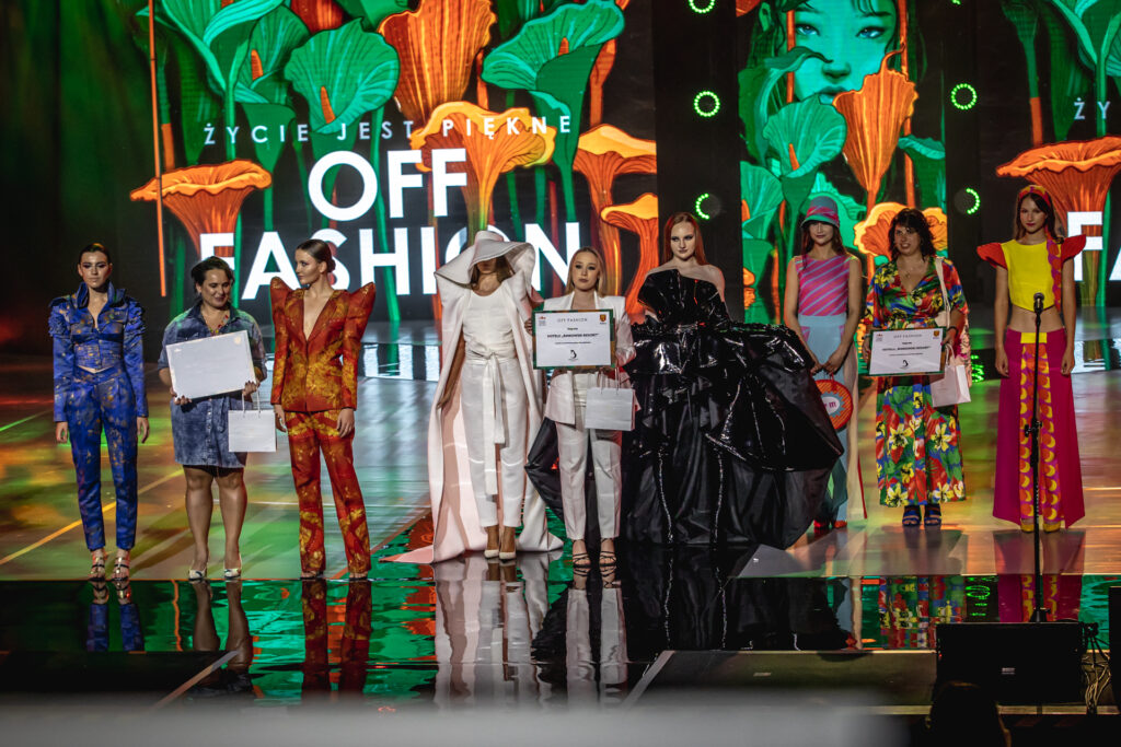 Zdjęcie. Trzy laureatki nagród 23. edycji konkursu OFF Fashion na scenie z ubranymi w zaprojektowane przez nie stroje modelkami.