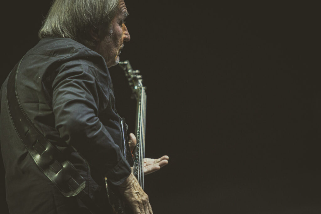 Zdjęcie. Mężczyzna gra na gitarze. Z tyłu - całkowita czerń sceny.