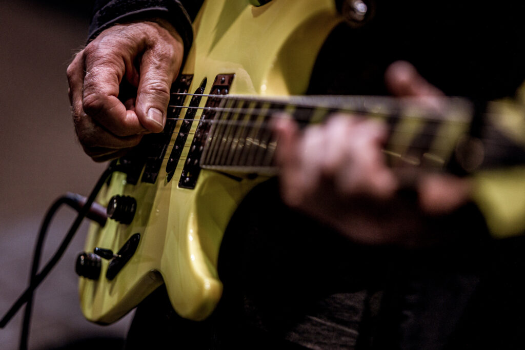 Zdjęcie zbliżenie na dłonie grające na żółtej gitarze.