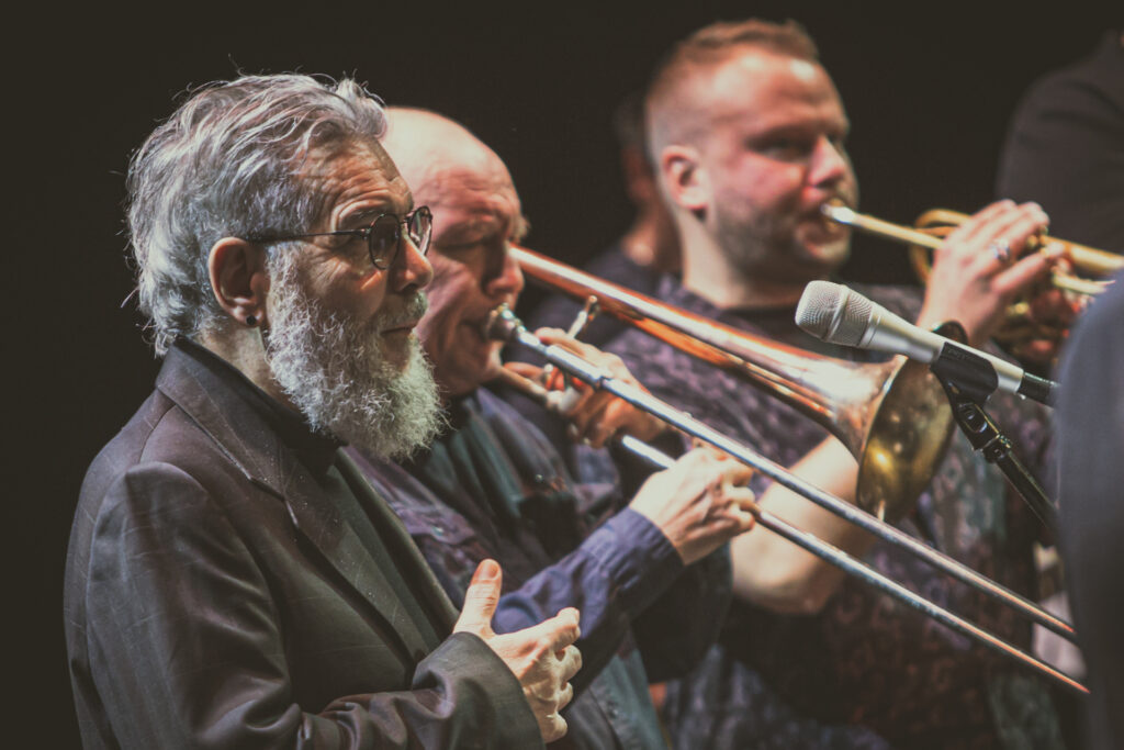 Zdjęcie. Koncrt Young Power New Edition podczas festiwalu Memorial to Miles Targi Kielce Jazz Festiwal. Na zdjęciu dwóch trębaczy. Przed nim Yorgos Skolias.