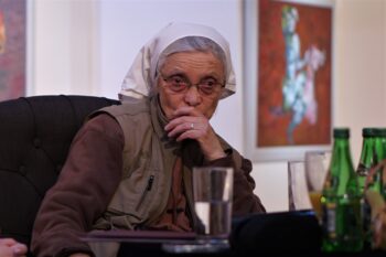 Zdjęcie. Gościni spotkania w Salonie Kobiet. Siostra Małgorzata Chmielewska ma włosy przykryte białą chustką, brązowy strój. Zamyślona patrzy przed siebie. Usta zasłania lewą ręką.