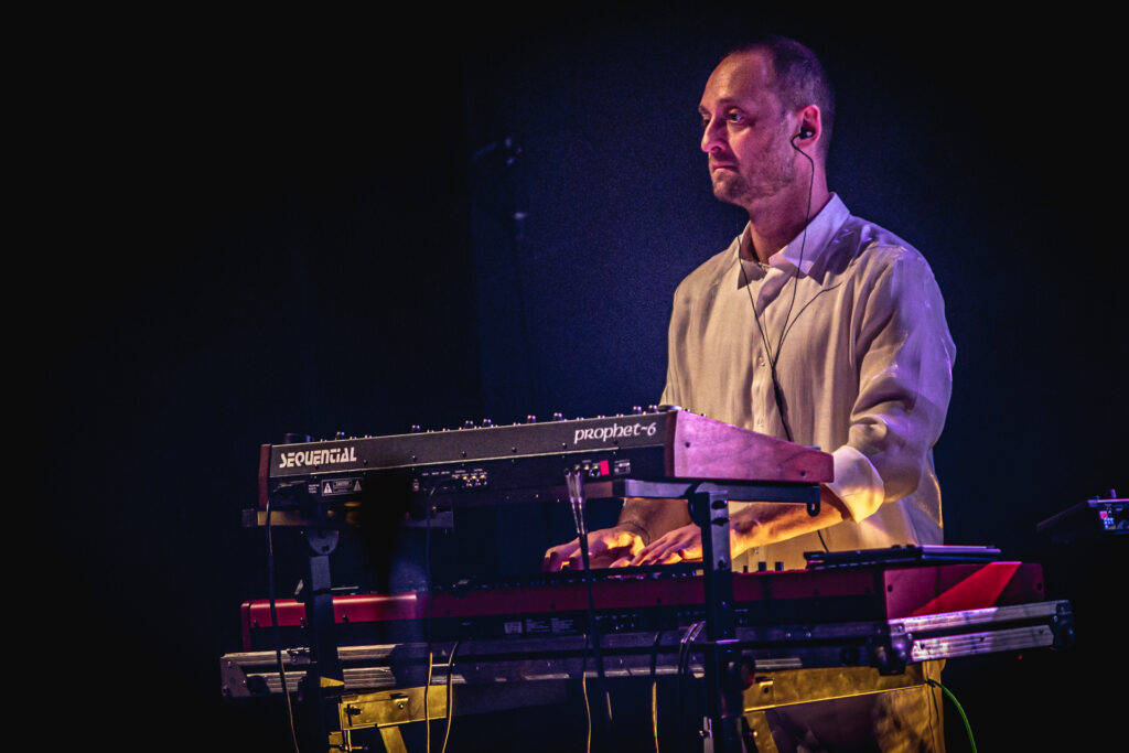 Zdjęcie. Mężczyzna z ciemną krótką brodą i wąsami gra na keyboardzie.