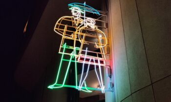 Zdjęcie. Neon: para pod parasolem świeci w nocy przy wejściu do Galerii Winda KCK.