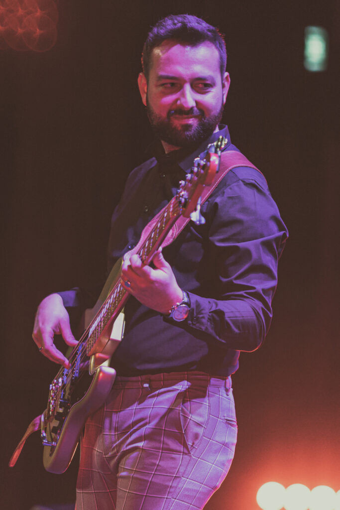 Zdjęcie. Mężczyzna gra na gitarze. Patrzy w bok z uśmiechem na twarzy.