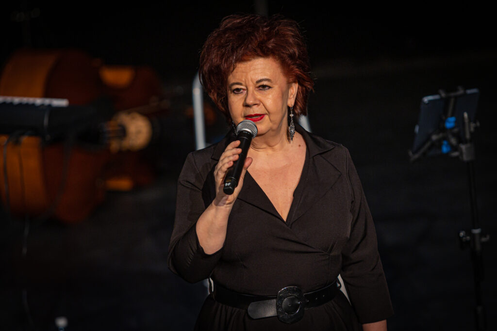 Zdjęcie. Kobieta w średnim wieku o kasztanowych włosach mówi do mikrofonu. To profesor Marzena Marczewska.