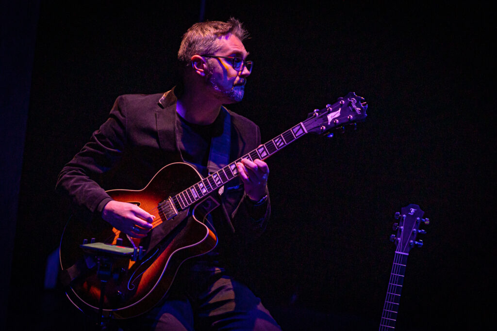 Zdjęcie. Oswietlony czerwonym światłem gitarzysta Wojciech Lipiński.