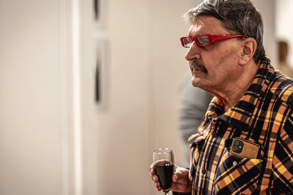 Zdjęcie. Starszy mężczyzna z okularami w czerwonych oprawkach i koszuli w żółto-czarna kratę przygląda się pracy Gudzowatego. To fotograf Echa Dnia Aleksander Piekarski.