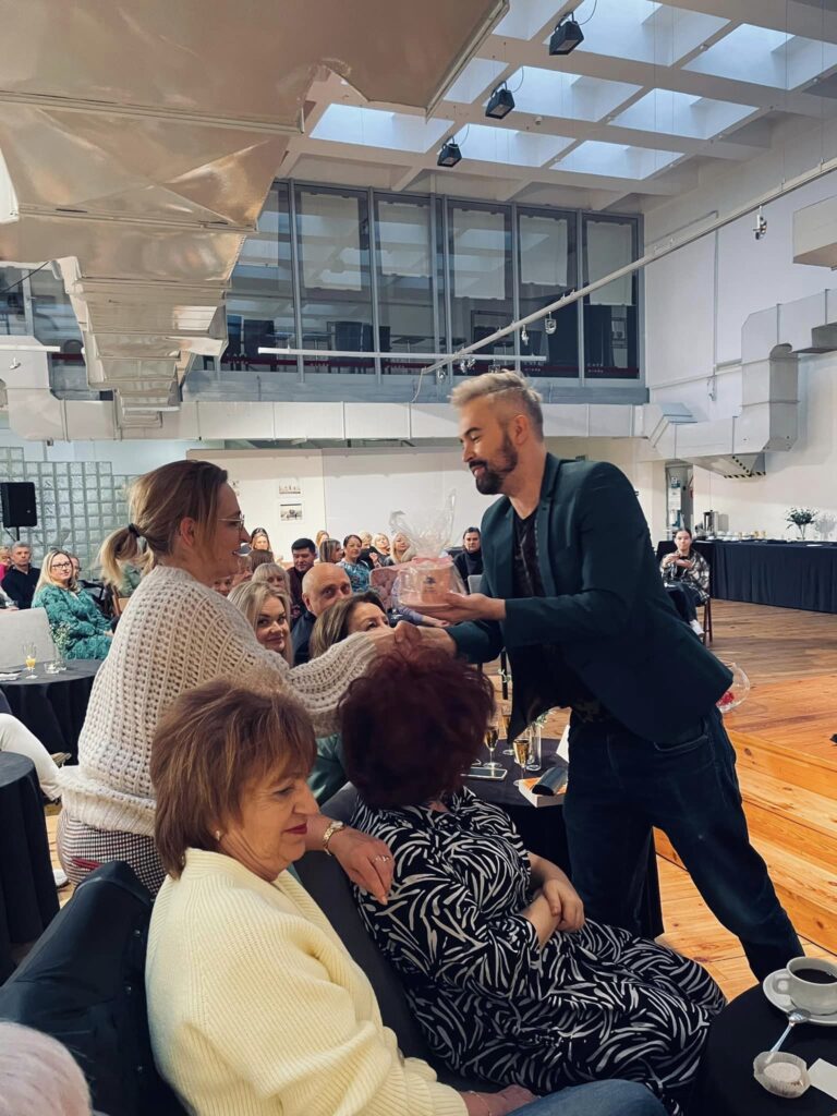 Zdjęcie. Wicedyrektor Artur Wijata podaje różową filiżankę zwyciężczyni losowania podczas Salonu Kobiet.