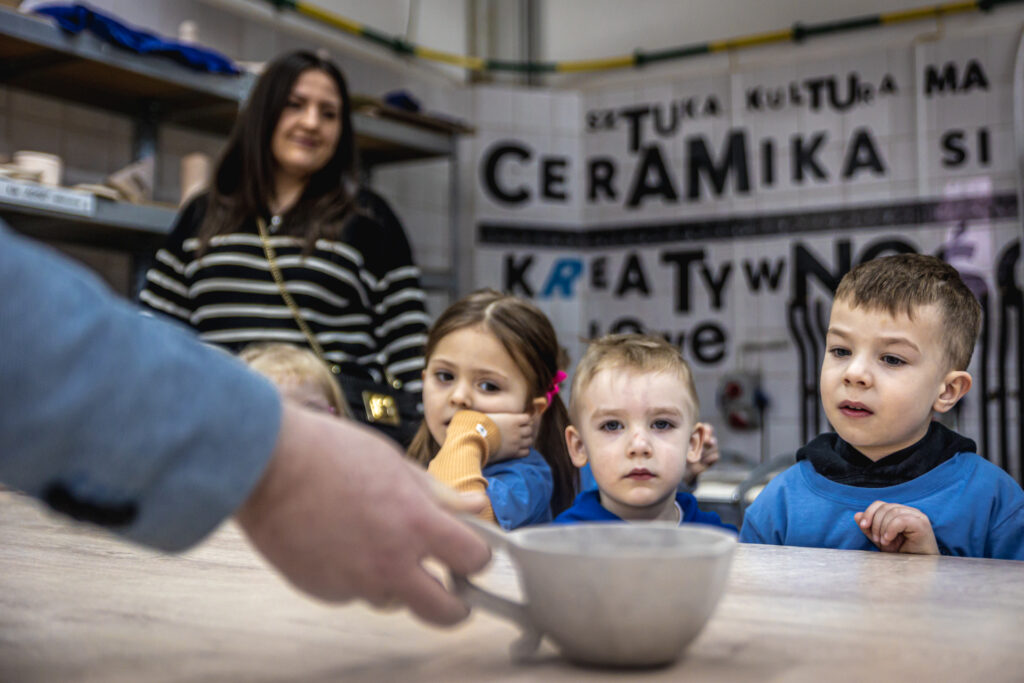 Zdjęcie. Przedszkolaki siedzą przy stole w pracowni ceramicznej. Przed nimi ceramiczna filiżanka.