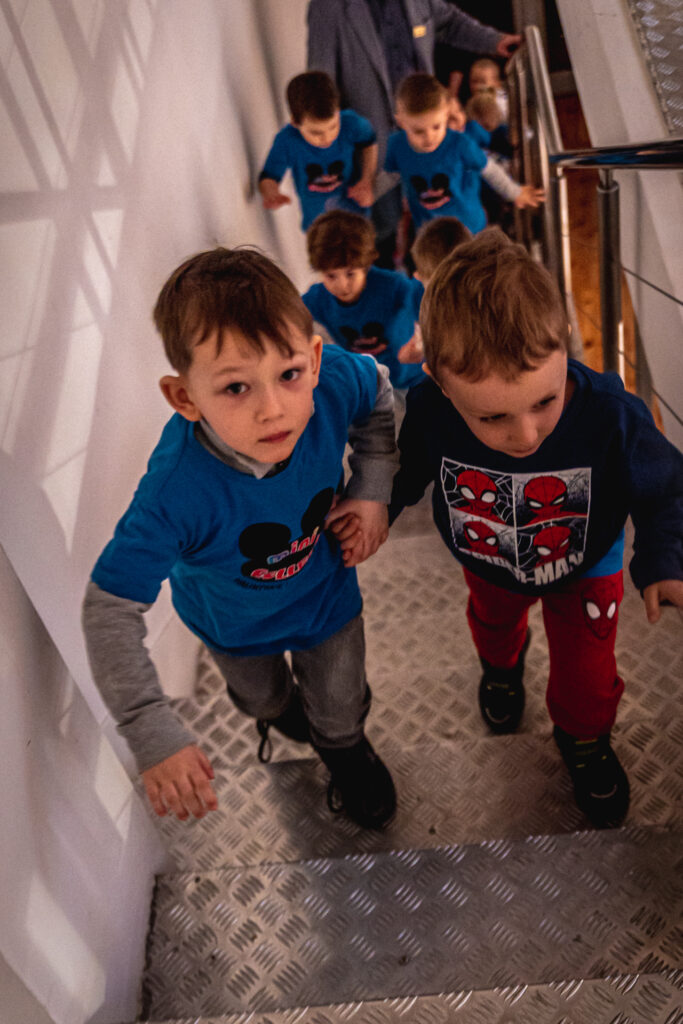 Zdjęcie. Grupa przedszkolaków wchodzi po wąskich metalowych schodach.