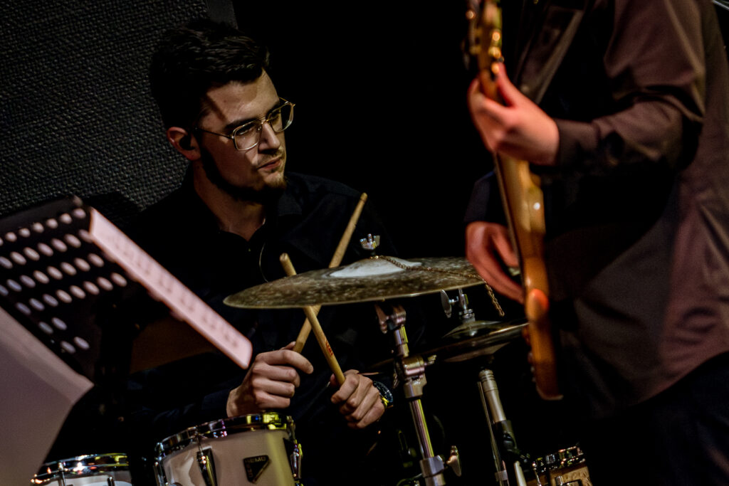 Zdjęcie. Perkusista w okularach gra na instrumencie.