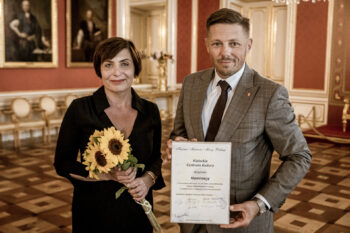 Zdjęcie. Sala Zamku Królewskiego w Warszawie. Dyrektor AugustynaNowacka i wiceprezydent Marcin Chłodnicki posują do zdjęcia z nominacją do tytułu Kuźnia Mistrzów Mowy Polskiej.
