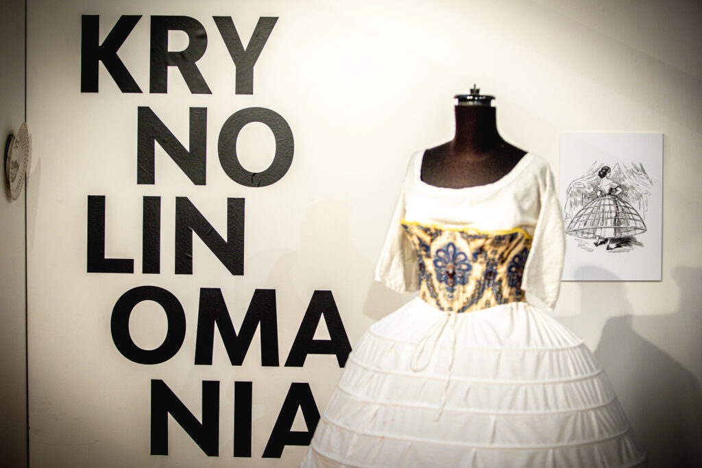 Zdjęcie. Wystawa "Krynolinomania" w Galerii "Winda". Na pierwszym planie halka z krynoliną. Z tyłu na ścianie napis: wielkie czarne litery: Krynolinomania.