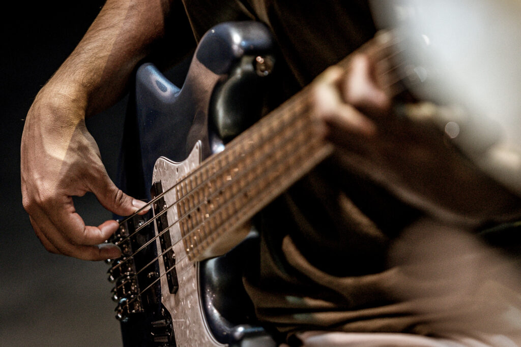 Zdjęcie. Dłonie grające na gitarze elektrycznej z pudłem w kolorze czarnym.