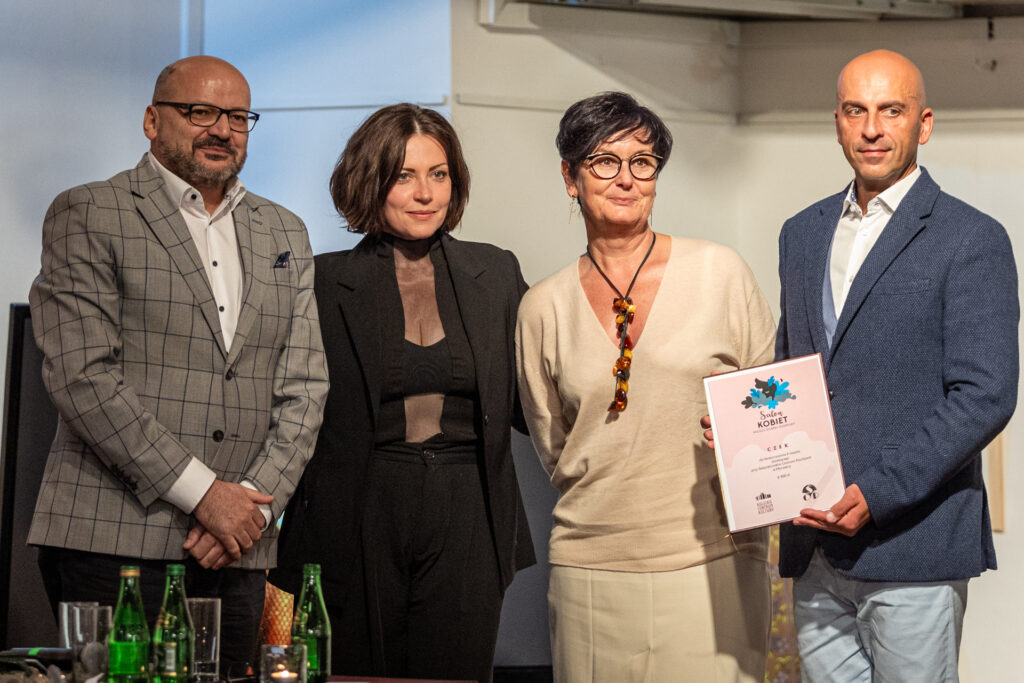 Zdjęcie. Aktorka Dagmara Domińczyk pozuje do zdjęcia z dyrektorm Szpitala Psychiatrycznego w Morawicy Piotrm Kiełbowskim i jego zastępcą Grzegirzem Kaletę. W ekipie jest także kobieta o krótkich włosach i okularach w ciemnych oprawkach ubrana w beżowy sweter i spódnicę. Grzegorz Kaleta trzyma w ręku czek. Wynagrodzenie za udział w Salonie Kobiet Dagmara Domińczyk przekazała na rzecz szpitala.
