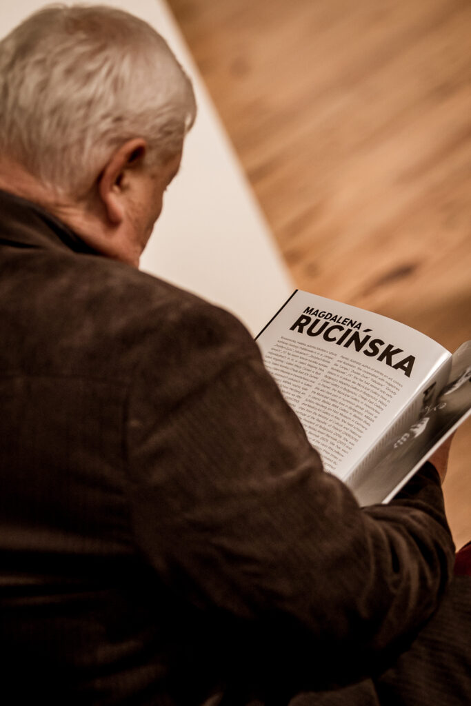 Zdjęcie. Starszy siwy mężczyzna w brązowej marynarce czyta. Na stronie jest duży napis Magdalena Rucińska. To katalog wystawy.