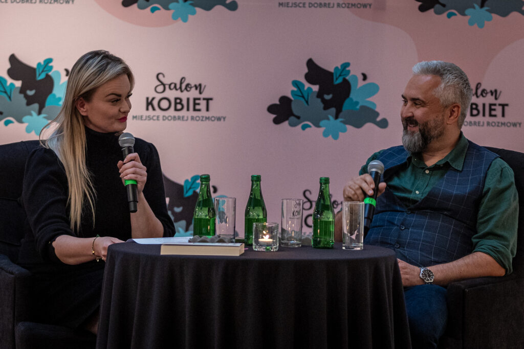 Zdjęcie. Dwójka ludzi siedzi przy stoliku. To Aleksandra Bielecka i doktor nerwica Marcin Matych podczas spotkania w Salonie Kobiet.