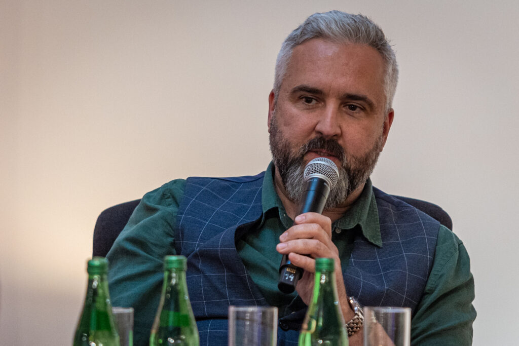 Zdjęcie. Szpakowaty mężczyzna z brodą mówi do mikrofonu. To dr Nerwica.