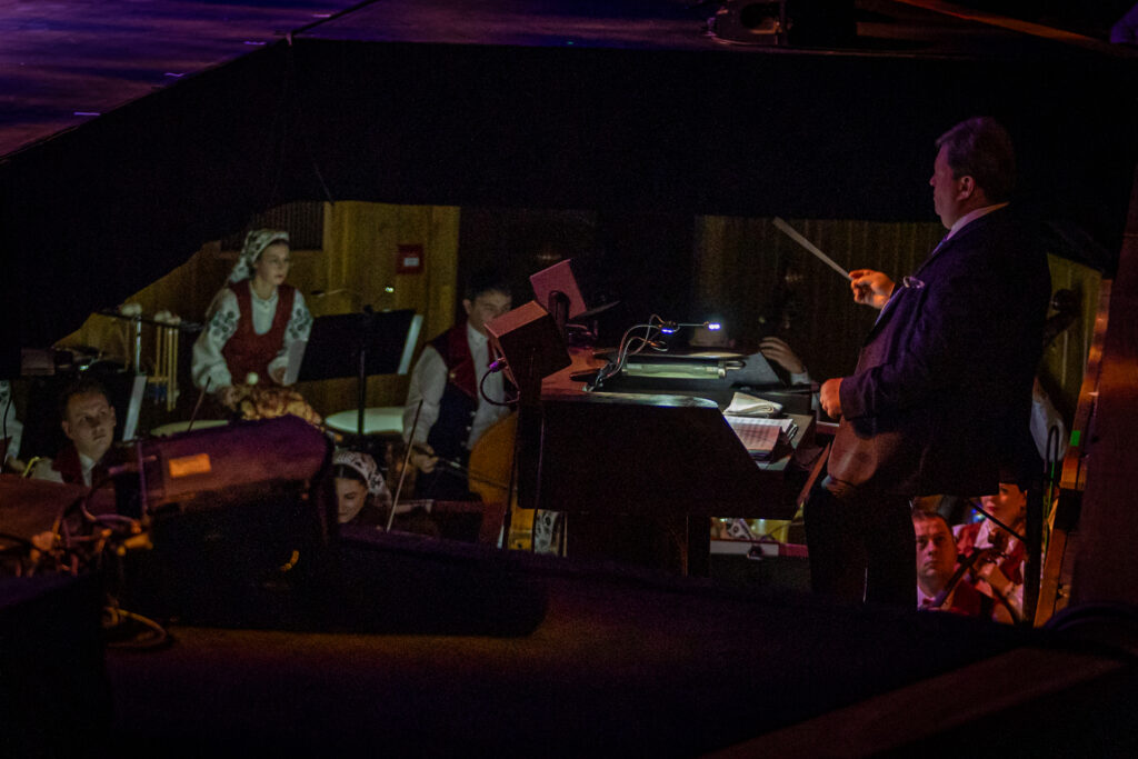 Zdjęcie. Dyrygent Jacek Boniecki i orkiestra w fosie Dużej Sceny Kieleckiego Centrum Kultury podczas koncertu zespołu "Mazowsze".