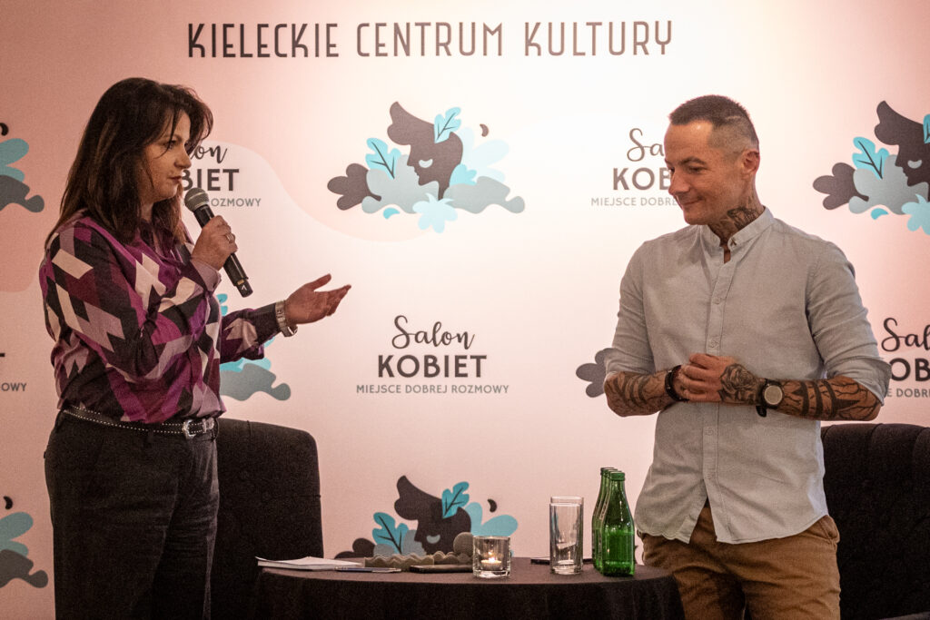 Zdjęcie. Kobieta i mężczyzna stoją na tle różowej ścianki z napisem Salon Konbiet. To prowadząca spotkanie brunetka Magdalena Fudala i Marcin Jóżefaciuk, pedagog z pasją i prowadzący program "Nastolatki rządzą kasą" w TVN.