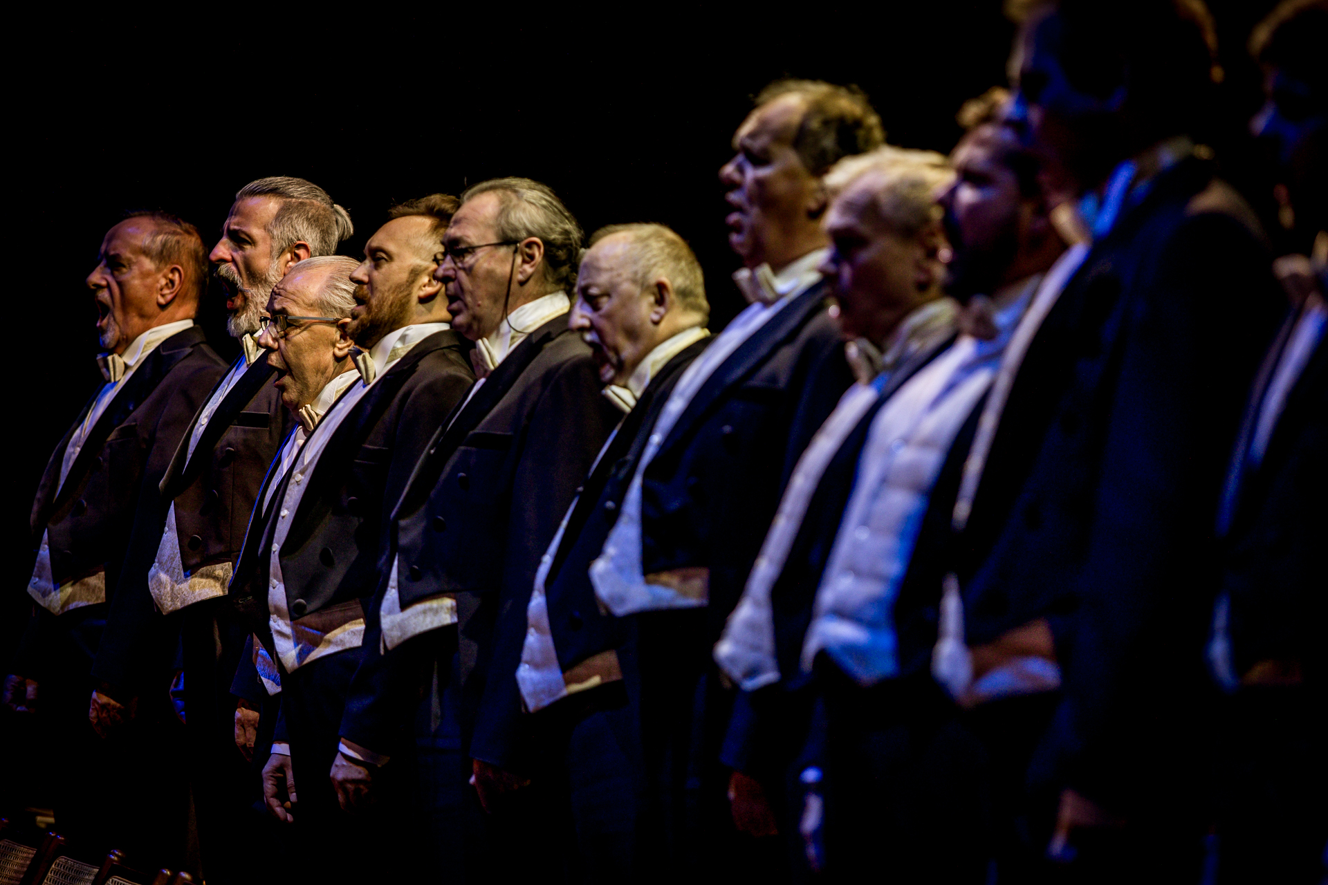 Zdjęcie. Rząd mężczyzn w średnim wieku ubranych we fraki. To chórzyści opery "Straszny dwór".