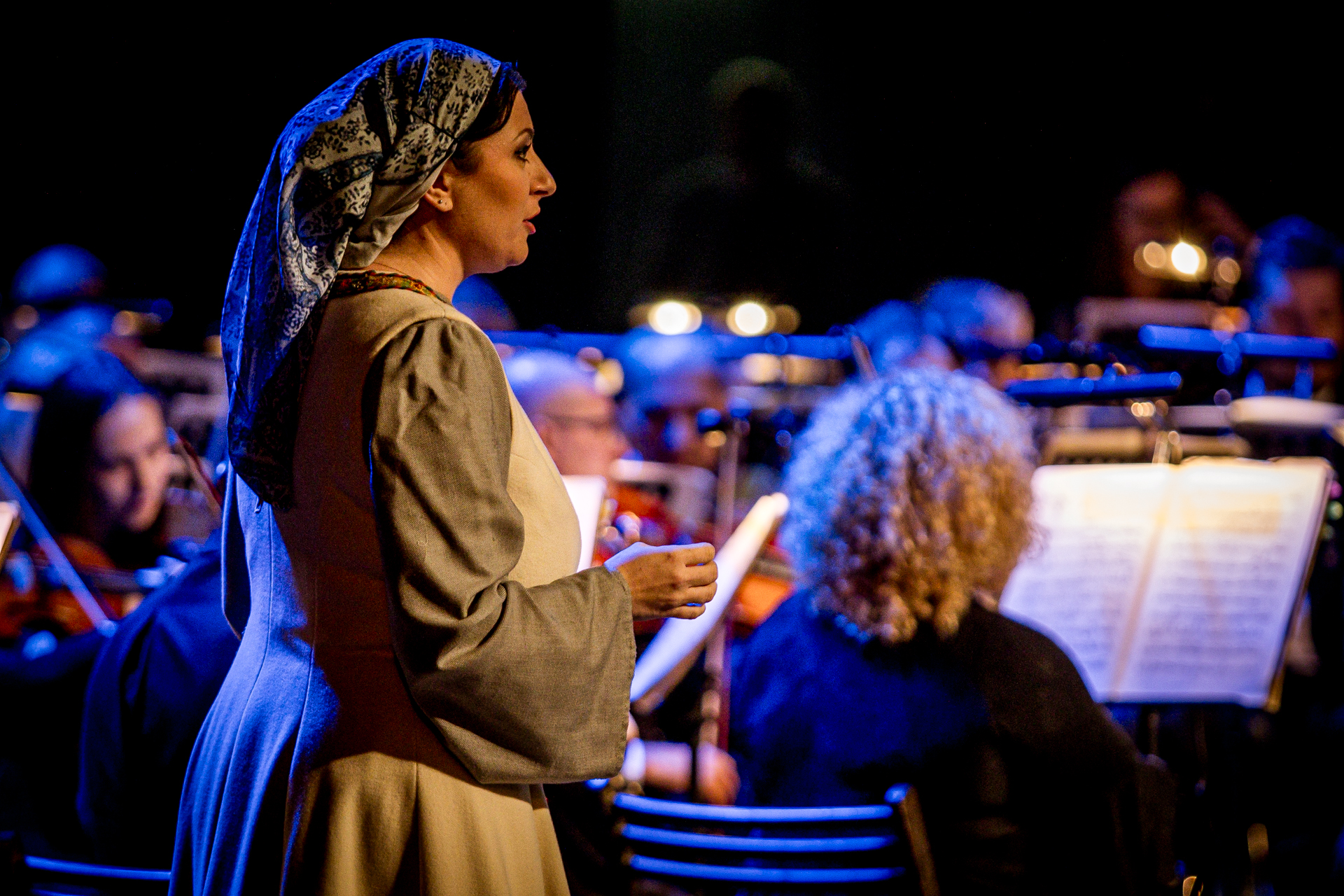 Zdjęcie. Kobieta w długiej beżowej sukni z chustką w drobny deseń na głowie śpiewa. To solistka opery "Straszny dwór"..