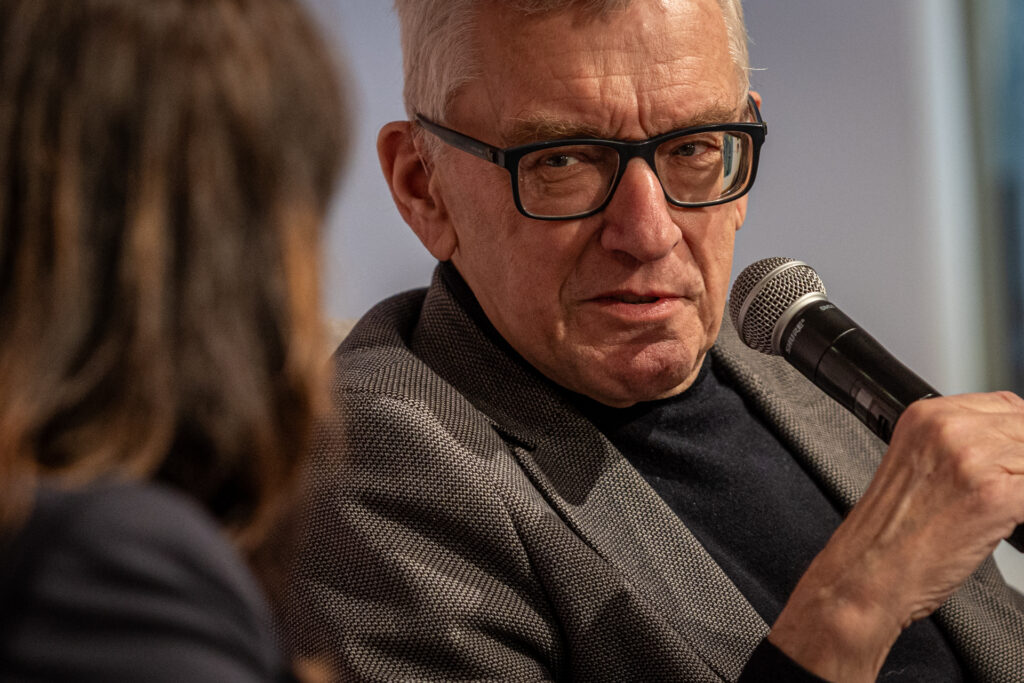 Zdjęcie. Siwy mężczyzna w okularach trzyma mikrofon. To Edward Rzepka podczas Salonu Kobiet.