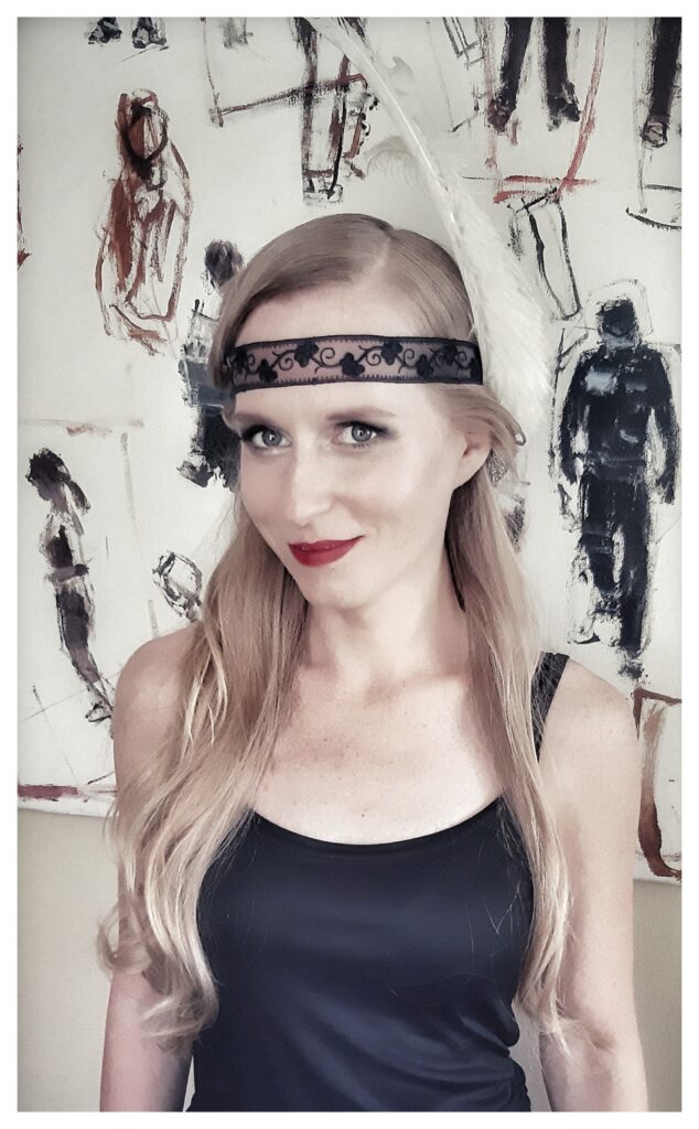 Zdjęcie. Szczupła blondynka o długich, rozpuszczonych włosach i koronkową przepaską na czole. To choreografka Angelika Skowronek.