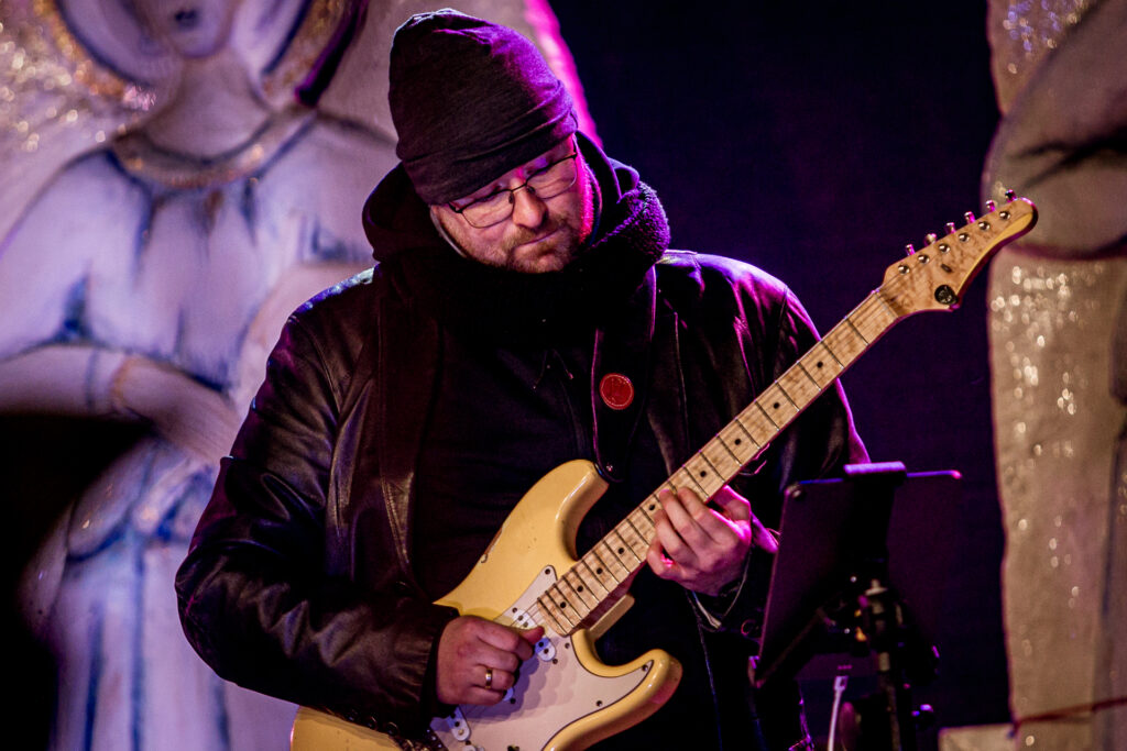 Zdjęcie. Gitarzysta z brodą i w okularach gra na gitarze.