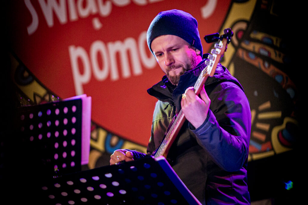 Zdjęcie. Gitarzysta gra na scenie na instrumencie. Patrzy w nuty.