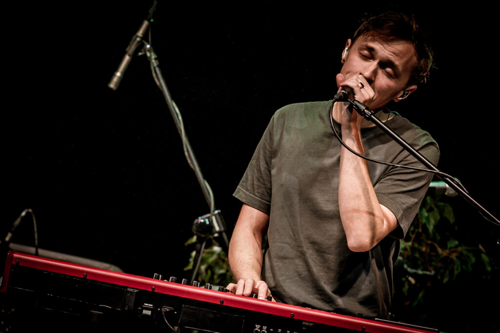 Zdjęcie. Koncert Podsłuchy. Mężczyzna stojący przed czerwonym keyboardem śpiewa do mikrofonu. To Patrick the Pan.