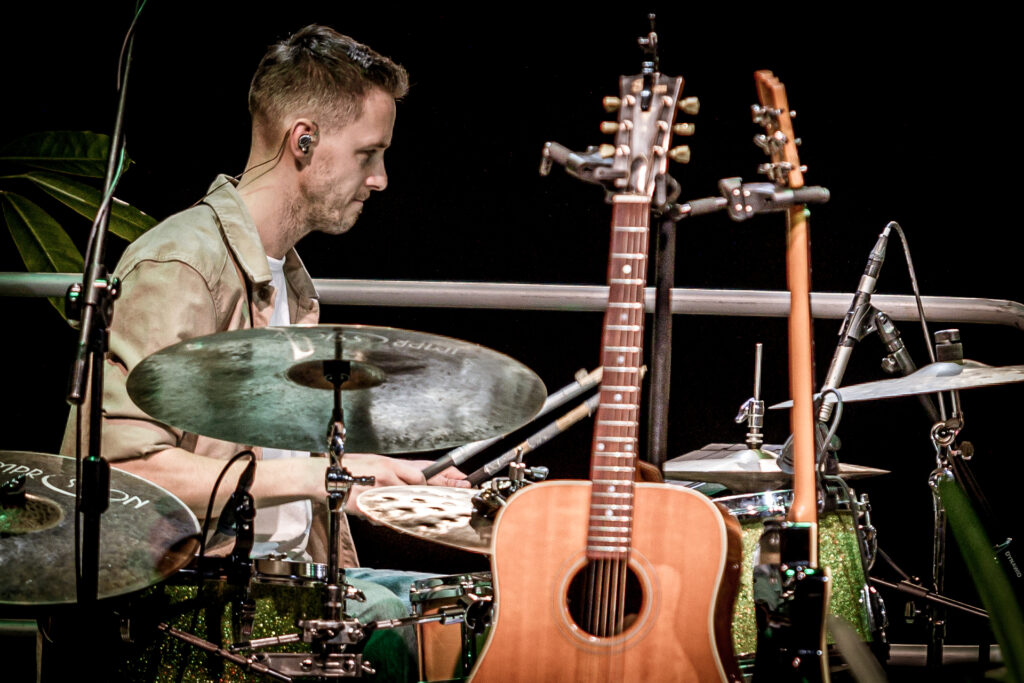 Zdjęcie. Koncert Podsłuchy. Mężczyzna z krótką brodą gra na perkusji. To muzyk zespołu Patrick the Pan. Przed perkusją dwie gitary oparte o stojaki.