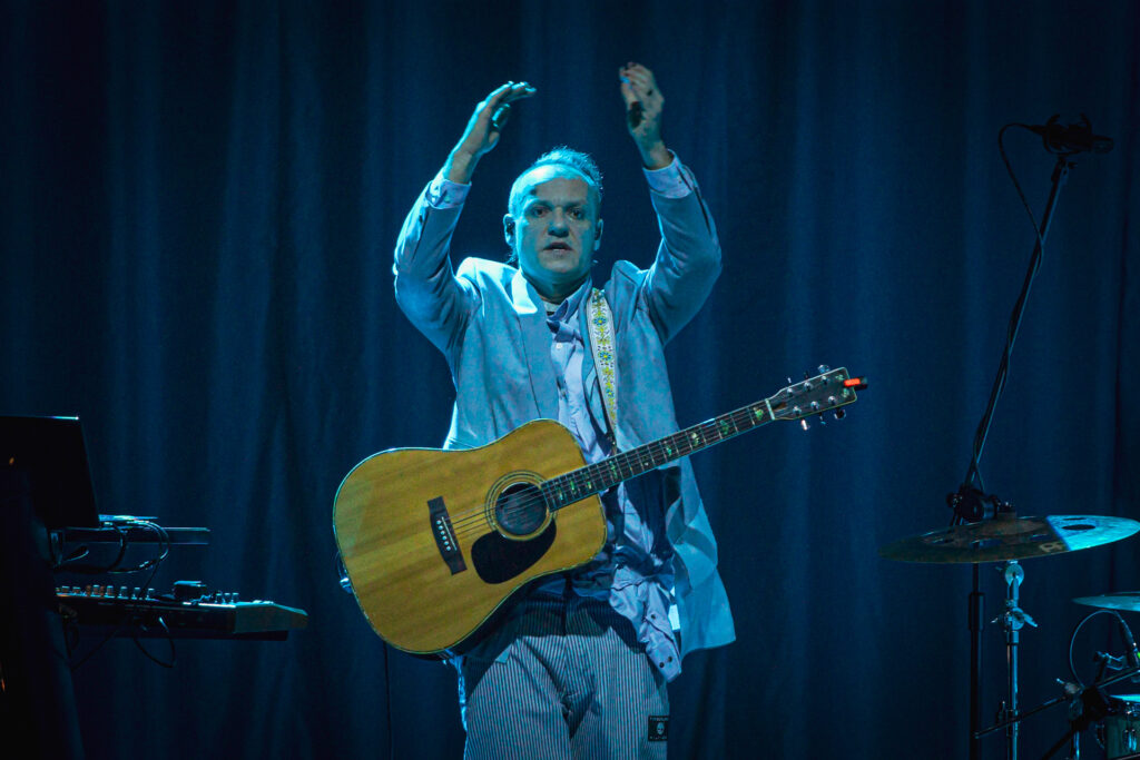 Zdjęcie. Gitarzysta zespołu Sorry Boys w jasnoniebieskiej marynarce klaszcze, trzymając ręce nad głową.