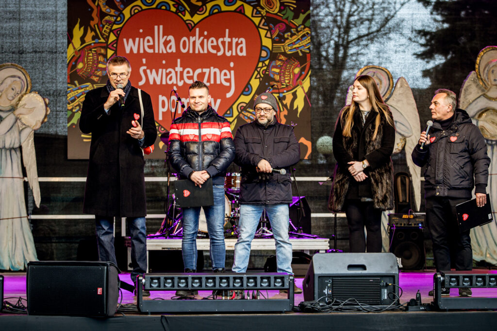 Zdjęcie. Plenerowa scena finału WOŚP pod KCK. Na scenie stoi 5 osób. Od lewej: prezydent Kielc Bogdan Wenta, dwóch panów w kurtkach i dżinsach, dyrektor KCK Agata Klimczak-Kołakowska i kolejny pan w czarnej kurtce.