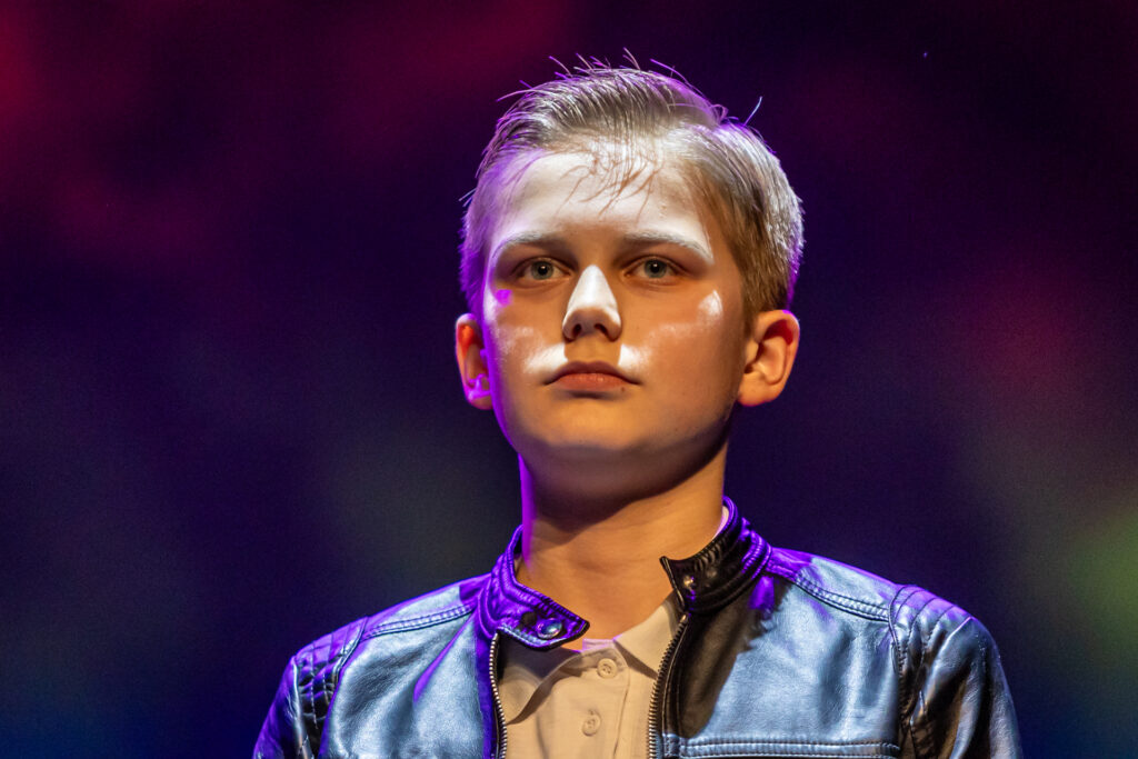 Zdjęcie. Młody chłopak o blond włosach w skórzanej kurtce patrzy przed siebie.