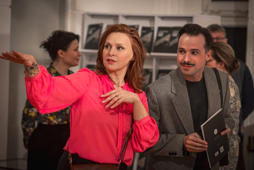 Zdjęcie. Paulina Holtz wskazuje mlodemu mężczyźnie z wąsami coś po prawej stronie. Mężczyzna to przedstawiciel marki Lilou.