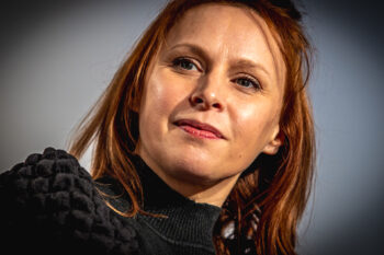 Zdjęcie. Ruda kobieta w czarnej bluzce patrzy przed siebie ze skupionym wyrazem twarzy. To Paulina Holtz, gościni Salonu Kobiet.