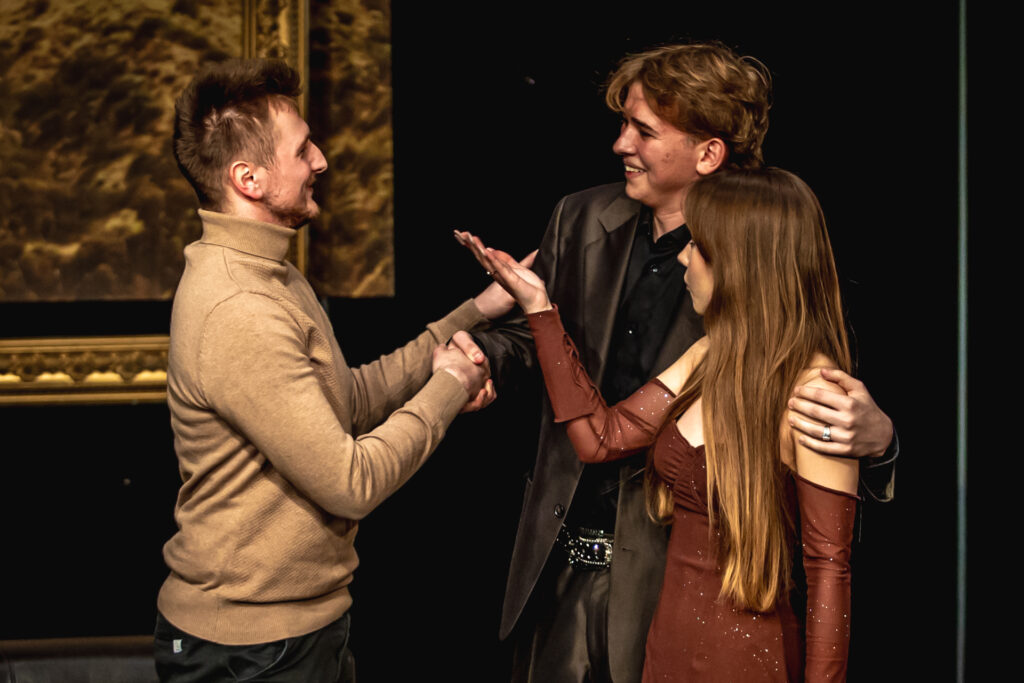 Zdjęcie. Teatr Pegaz. Trójka ludzi: dwóch chłopaków i jedna dziewczyna stoją wblisko siebie w kółku i rozmawiaja. Chłopaki się uśmiechają, kobieta ma poważną minę i wyciąga rękę przed siebie.