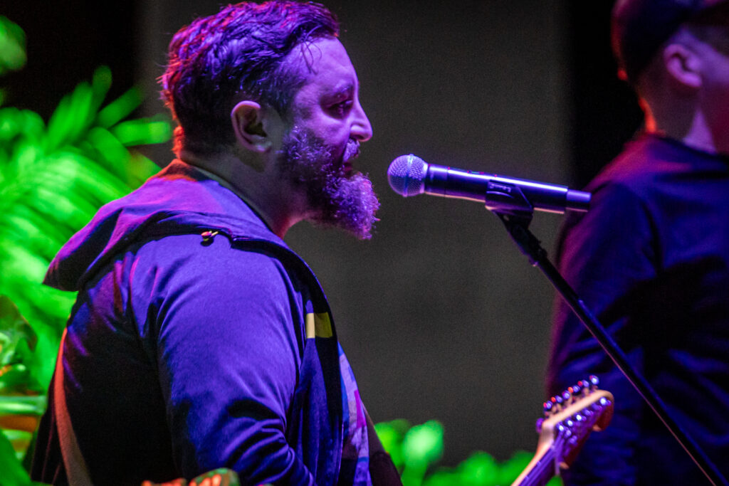Zdjęcie. Gruby mężczyzna z długa brodą w bluzie z kapturem gra na gitarze. to muzyk zespołu Hurt.