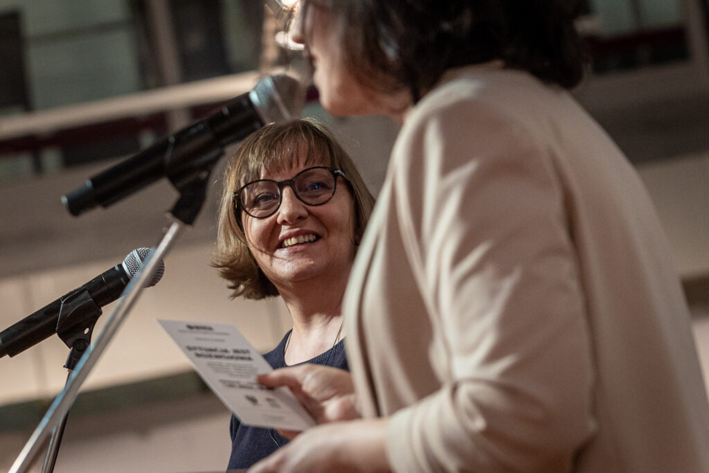Zdjęcie. Wernisaż wystawy "Sytuacja jest rozwojowa". Kobieta w jasnej marynarce mówi do mikrofonu. To Daria Maroń-Ptak. Przygląda się jej druga uśmiechnięta kobieta. To Iwona Stachura.