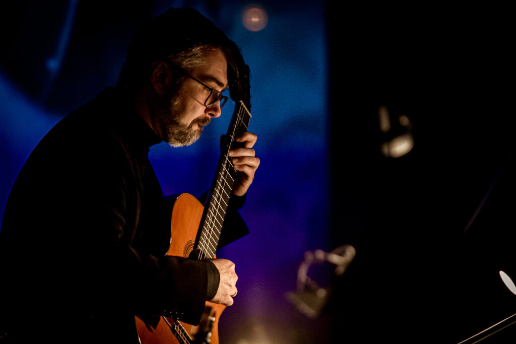 Zdjęcie. Muzyk w okularach gra na gitarze. To Wojciech Lipiński.