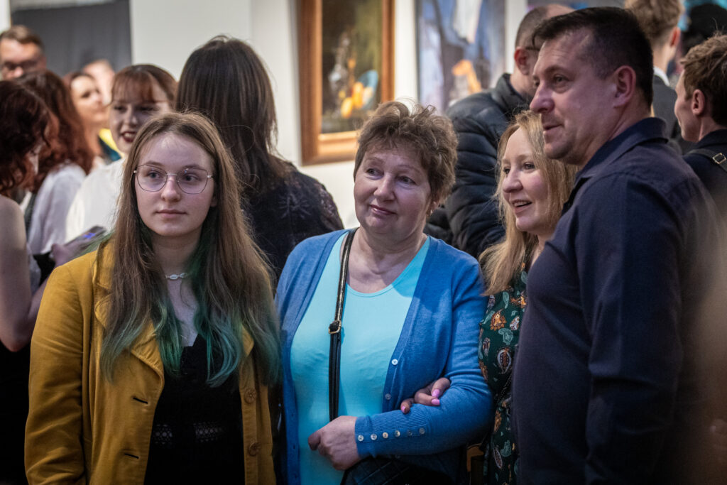Zdjęcie. Grupa ludzi: trzy kobiety i jeden mężczyzna stoją blisko siebie i patrzą w jednym kierunku.