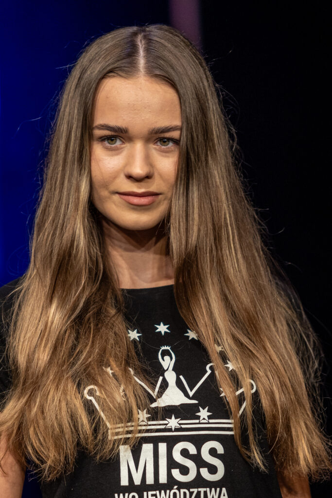 Zdjęcie. Ciemna blondynka o regularnych rysach twarzy i pięknych ustach patrzy przed siebie z delikatnym uśmiechem.